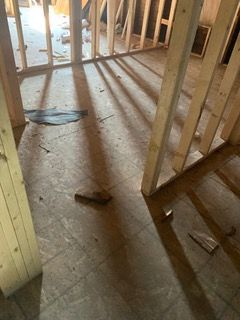 Exposed wooden floor joists in a partially demolished room with construction debris on the floor.