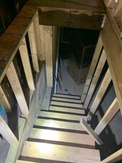 Dimly lit wooden staircase descending into a dark basement or attic space.