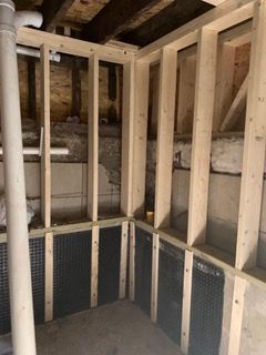 Unfinished basement wall framing with exposed studs, insulation, and a concrete floor