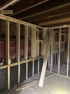 Unfinished basement with exposed wooden framing, insulation, and a concrete floor, with boards leaning against the wall