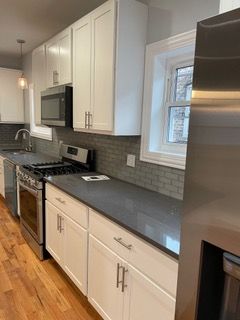 Modern kitchen with white cabinets, gray countertops, stainless steel appliances, and hardwood floors