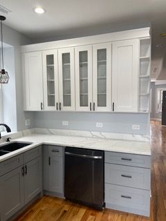 Modern kitchen with white upper cabinets, gray lower cabinets, black dishwasher, and light countertops