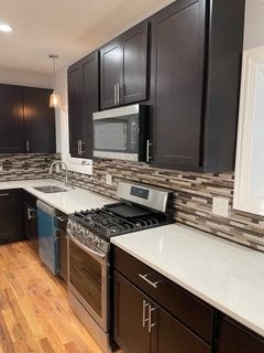 Modern kitchen with dark cabinets, stainless steel stove, and white countertops with mosaic backsplash