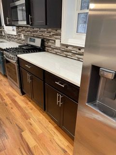 Modern kitchen with dark cabinets, stainless steel appliances, white countertops, and wood floors