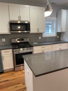 Modern kitchen with gray countertops, white cabinets, stainless steel appliances, and a central island