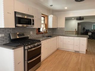 Modern kitchen with stainless steel appliances, white cabinets, black countertops, and wood flooring