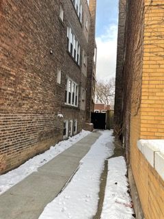 Narrow snowy alley between brick buildings with a cleared walkway leading to a gate at the end