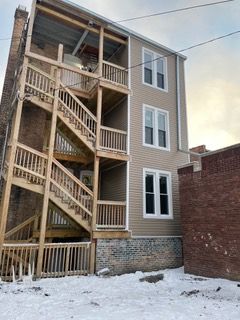 Snow-covered alley beside a tan apartment building with exterior wooden stairs and balconies