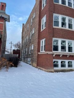 Snow-covered alley beside a red brick apartment building with white-trimmed windows