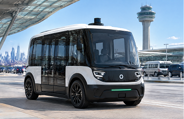 Self-driving shuttle van at an airport terminal, with tower and skyline in the background