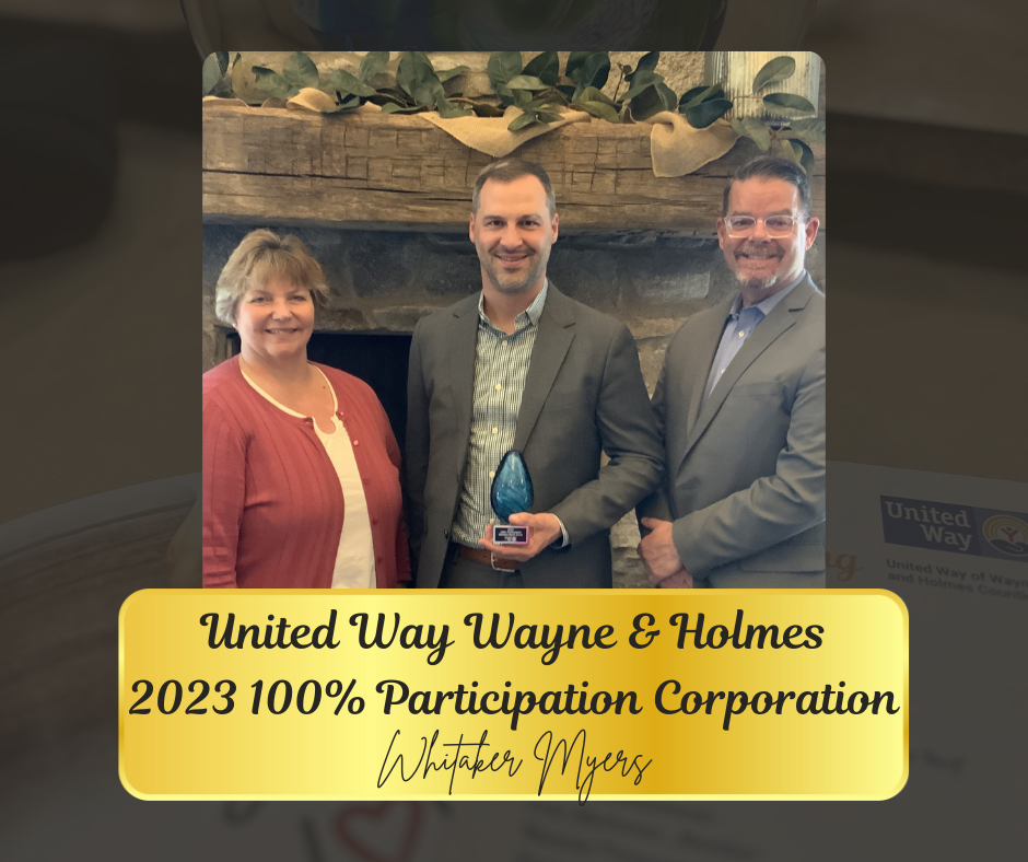 Three people in front of a fireplace, one holding an award, celebrating 100% participation with United Way.
