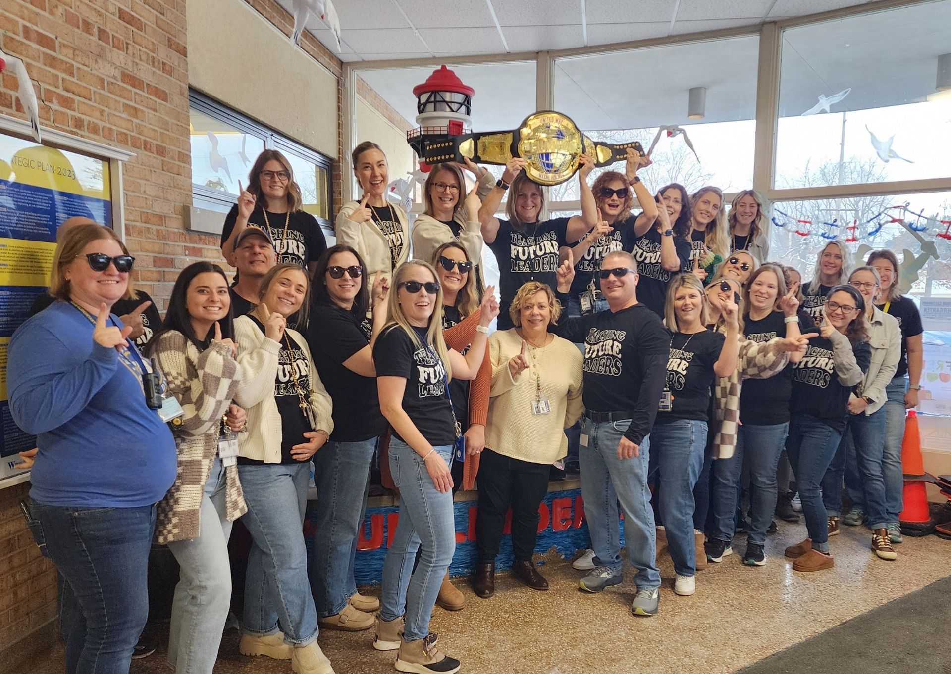 Group of people holding a championship belt, wearing sunglasses, posing inside a school.