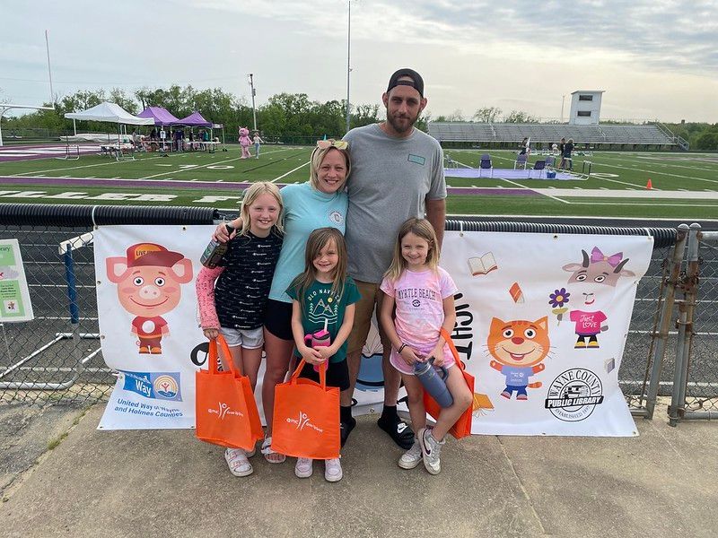 Family posing with orange bags in front of a banner at an outdoor track.