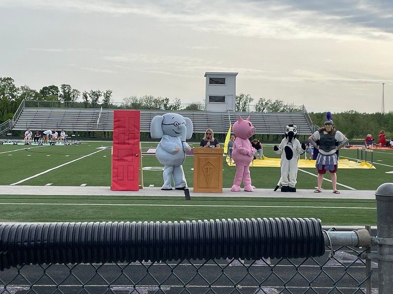 Five costumed characters on a field: a door, elephant, judge, pig, zebra, and band member.