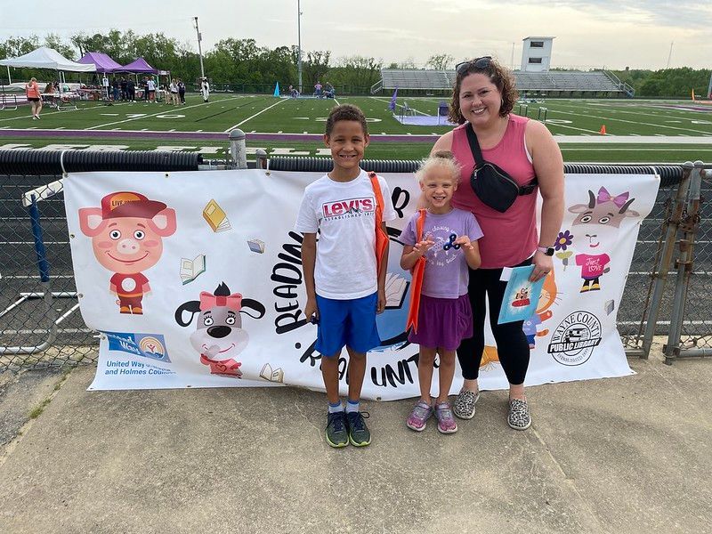 A woman and two children stand near a banner that says 