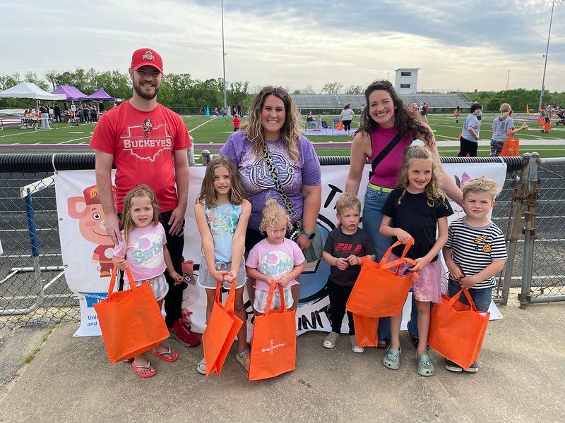 Group of people and children with orange bags posing on a track.