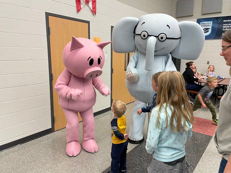 Pig and elephant mascots with children in a school hallway.