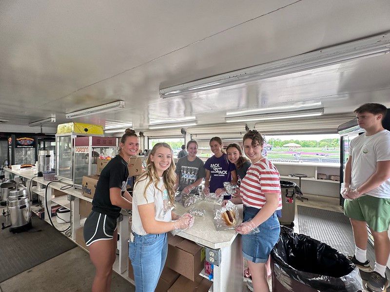 Group of people preparing food inside a concession stand. They are smiling and
working together.