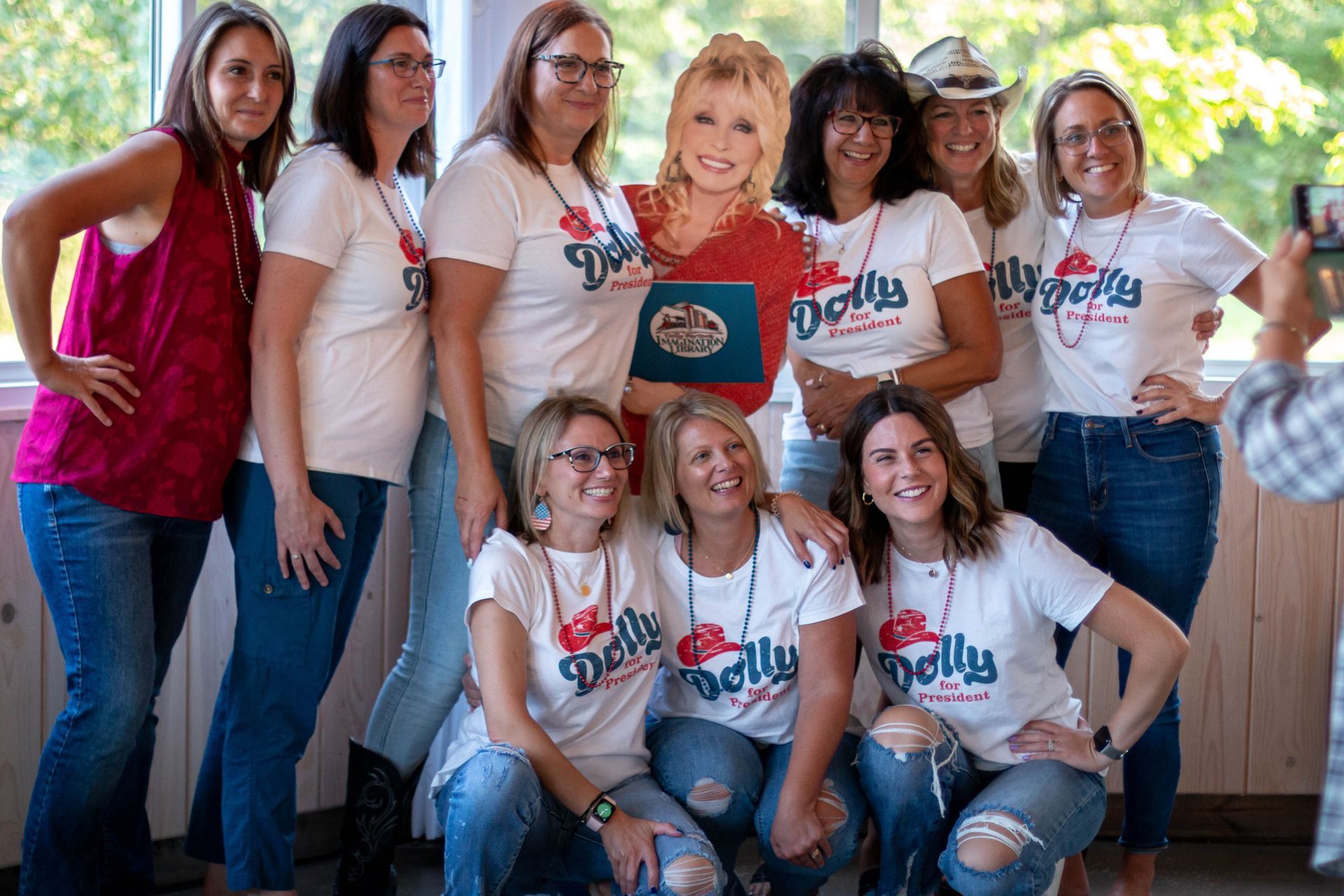 Group of women pose with a Dolly Parton cardboard cutout, wearing matching t-shirts and jeans.