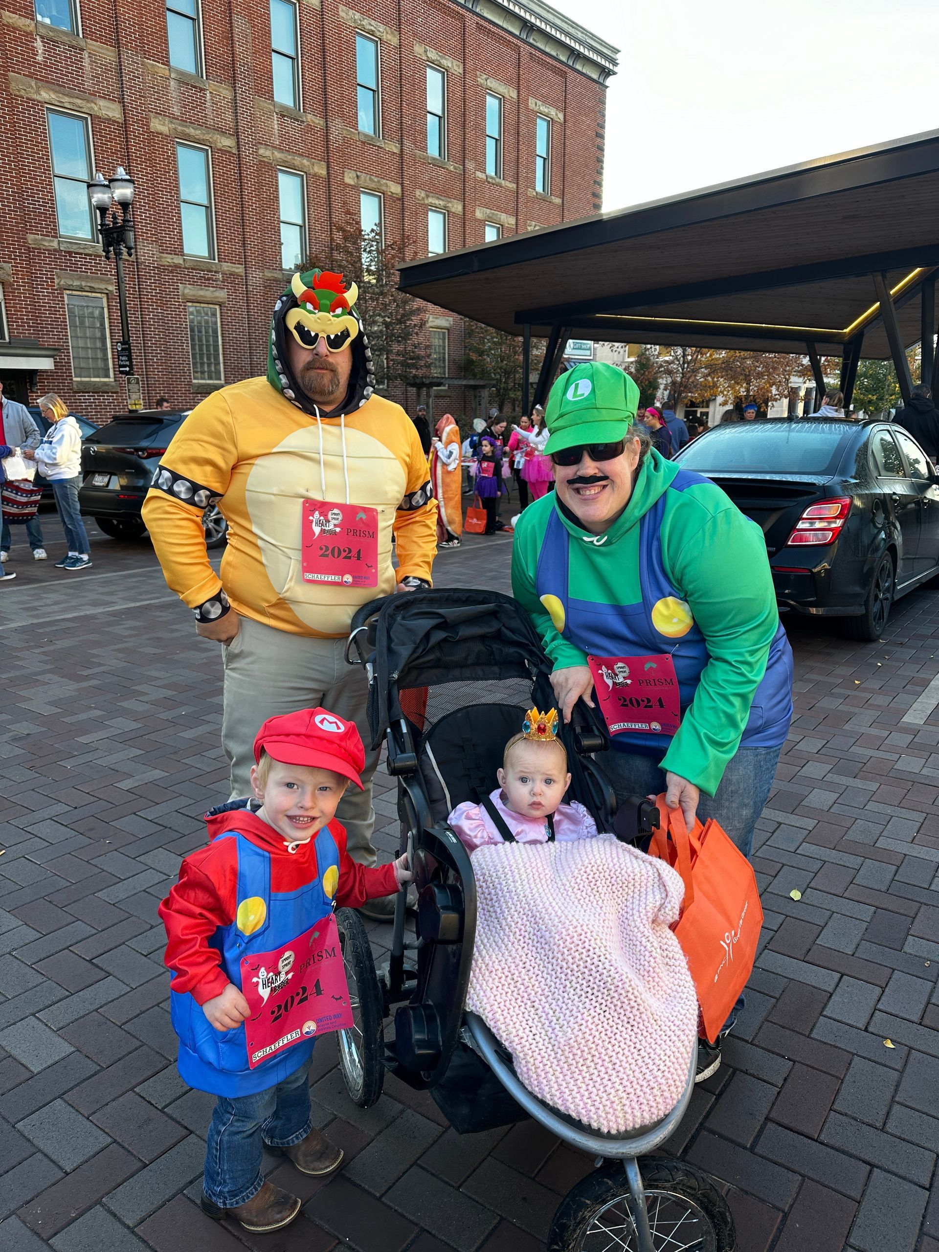 Family in Mario-themed costumes: Bowser, Luigi, Mario, and a baby in a stroller.