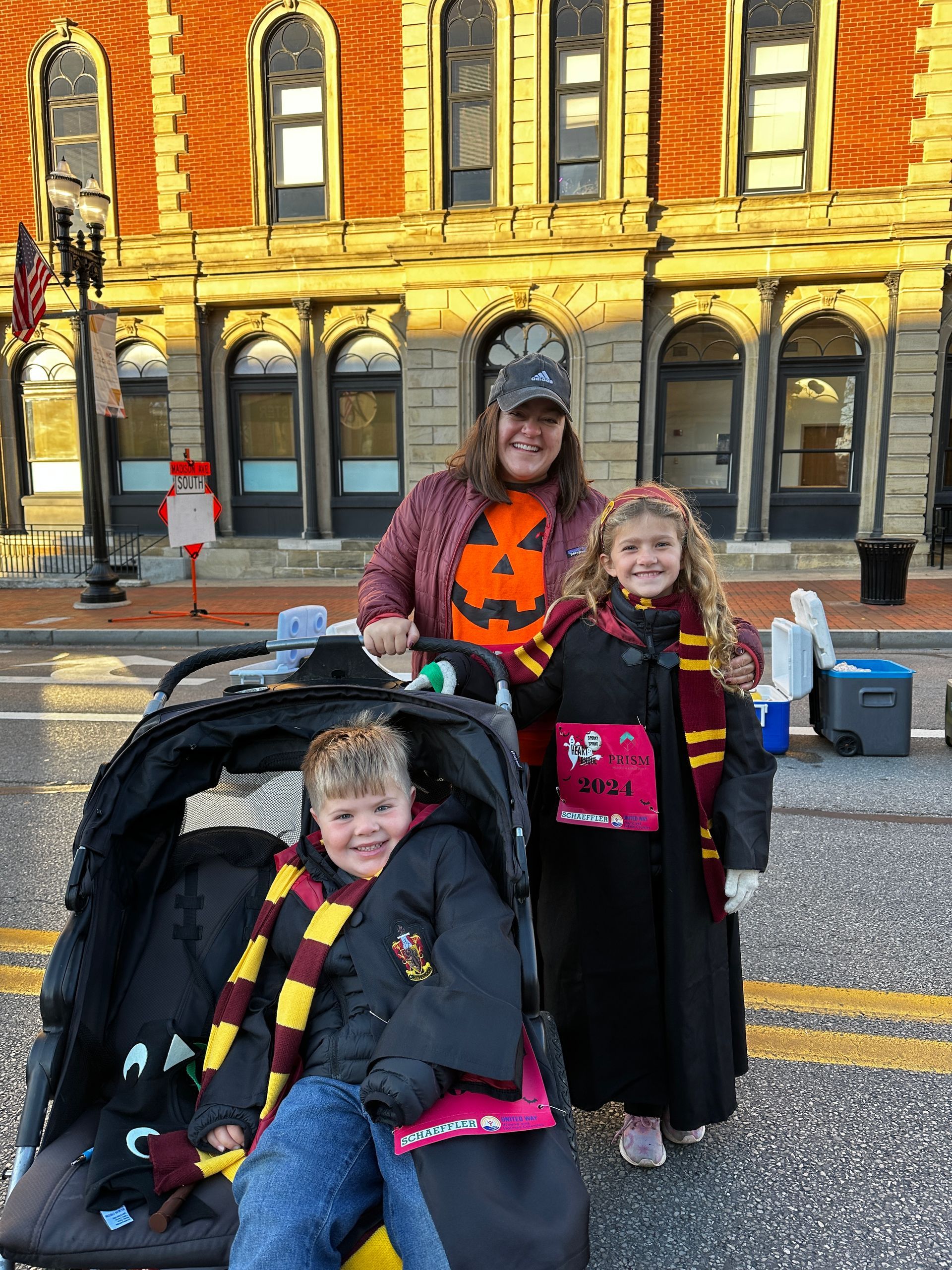 A woman and two children in Harry Potter costumes pose outdoors in front of a brick building.