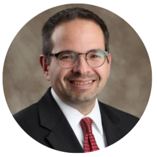 Man in glasses and suit smiling, likely a professional headshot.