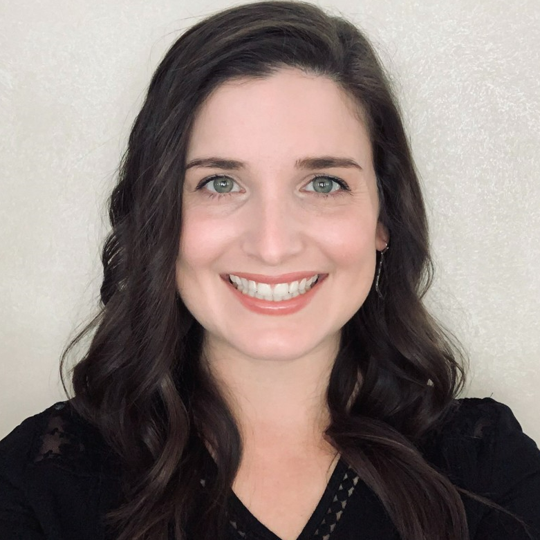 Woman with dark hair smiles, looking at the camera. She's wearing a black top.