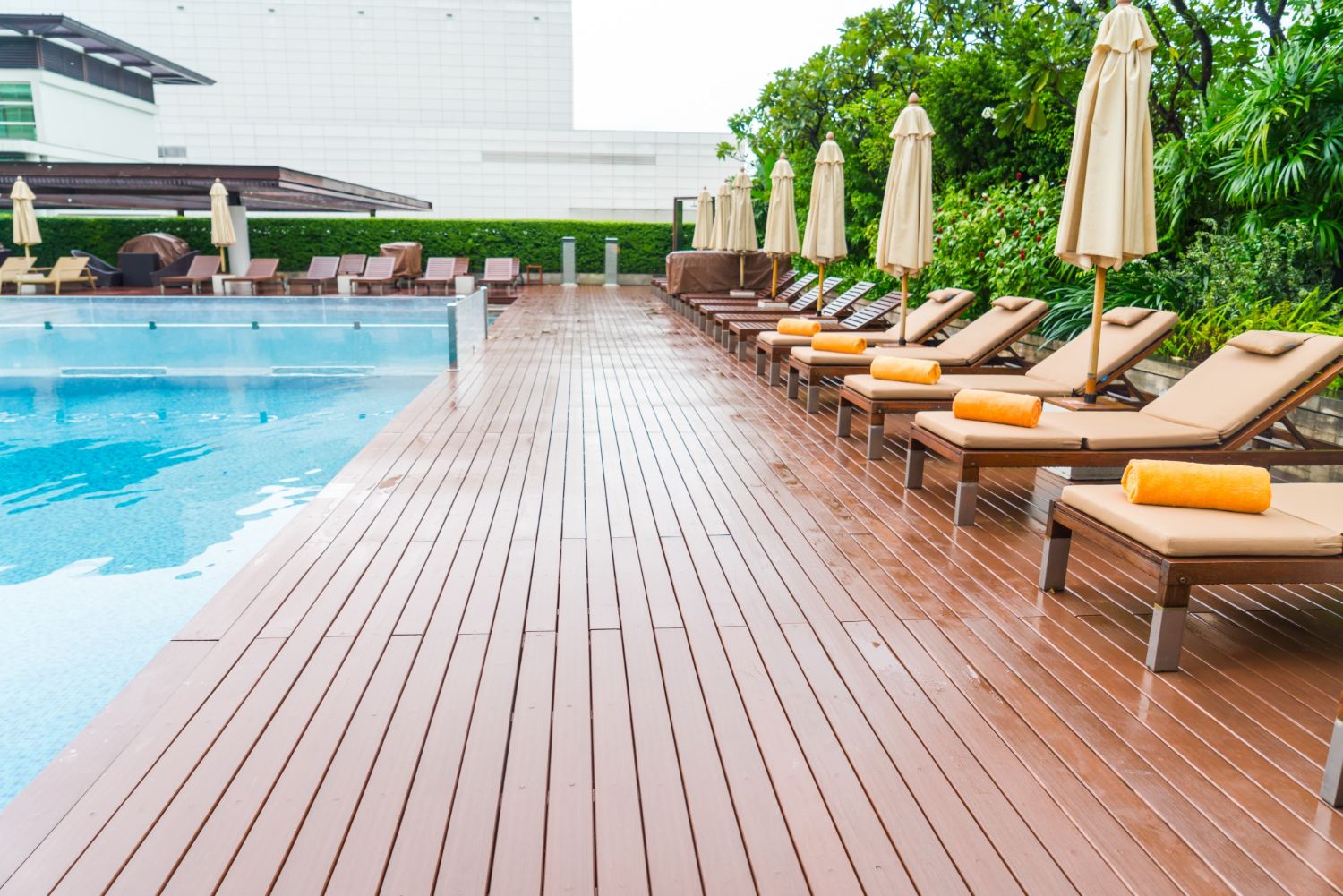 Poolside scene with wooden deck, lounge chairs, umbrellas, and pool with blue water.