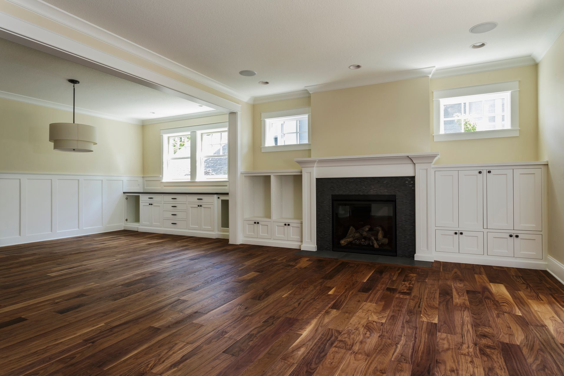 Empty living room with wood floor, fireplace, built-in cabinets, and large windows.