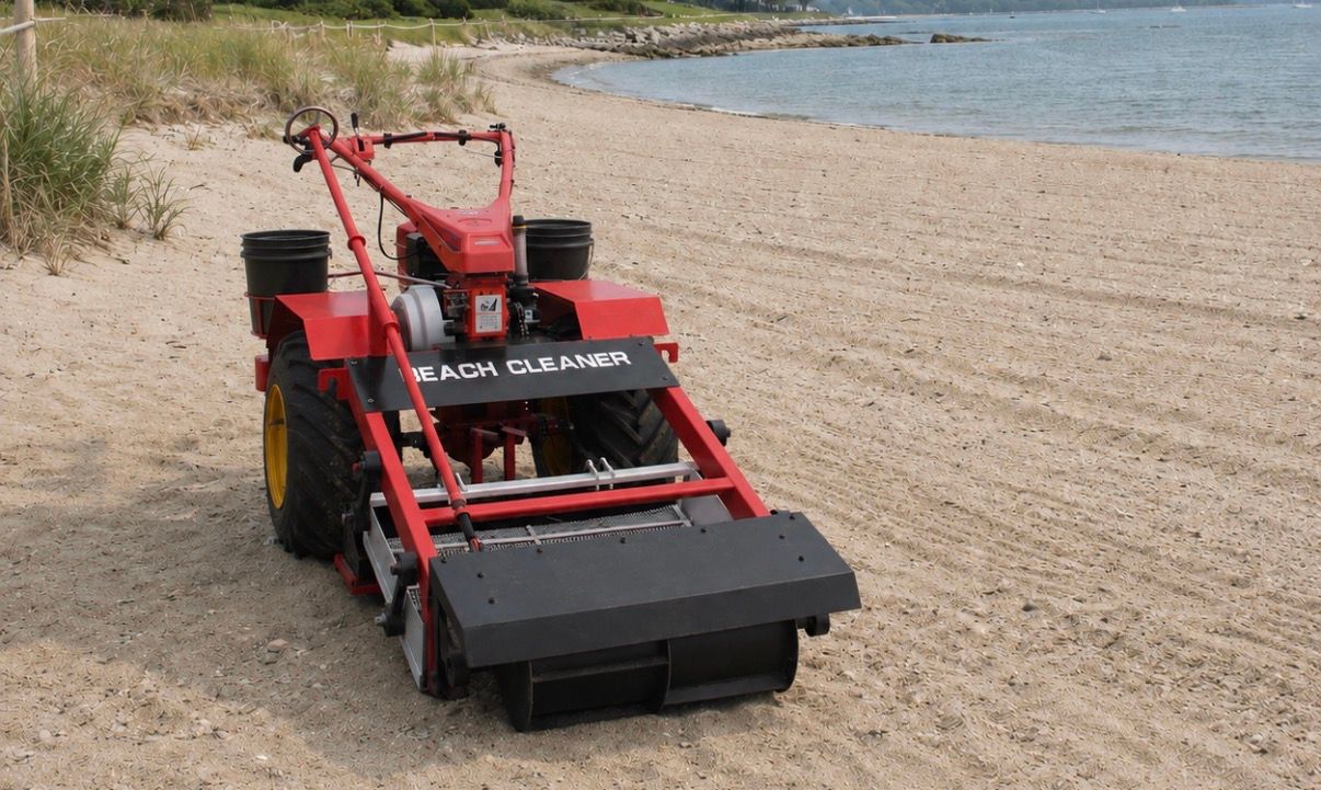 Red track-styled beach cleaning machine on a sandy shoreline beside calm water