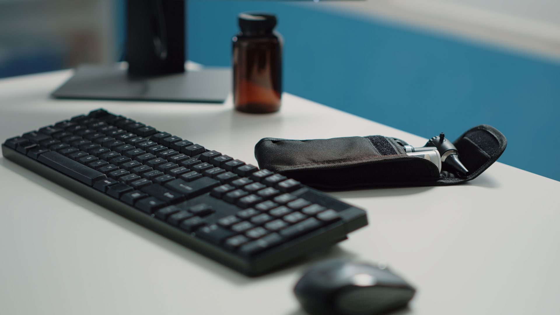 Black keyboard, mouse, and open leather case with tools sit on a white desk near a brown pill bottle.