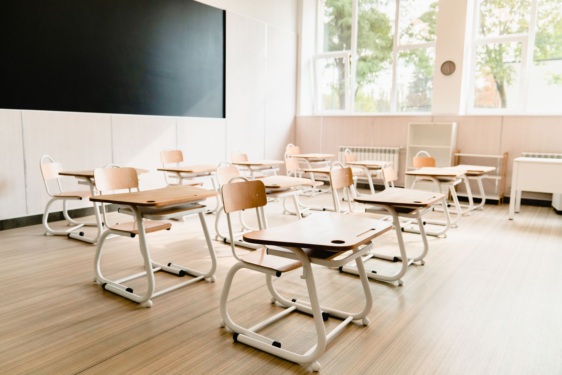 Empty classroom with desks, chairs, chalkboard, and large windows.
