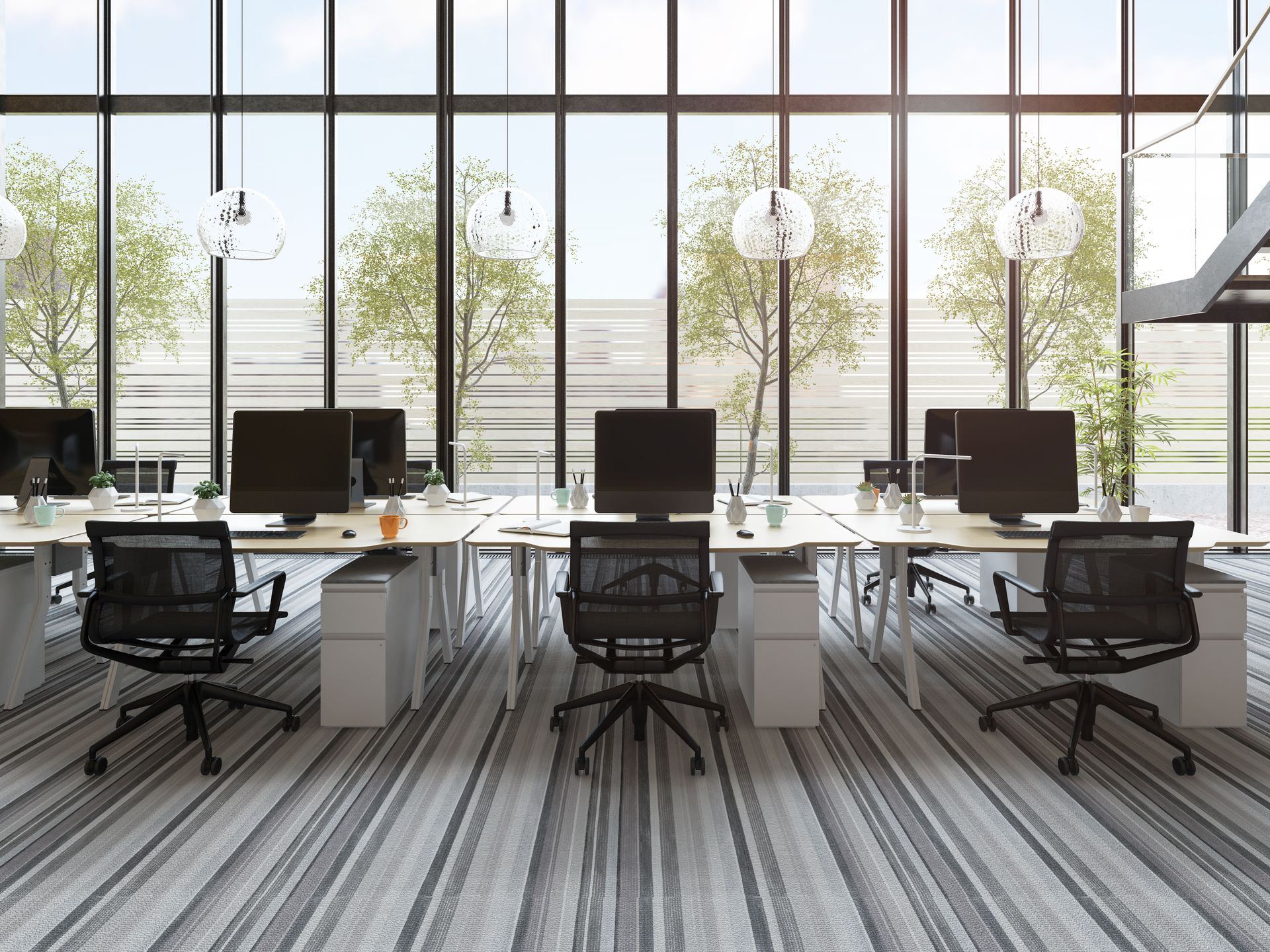 Modern office with several desks, chairs, computers, and a large window with a view of trees.