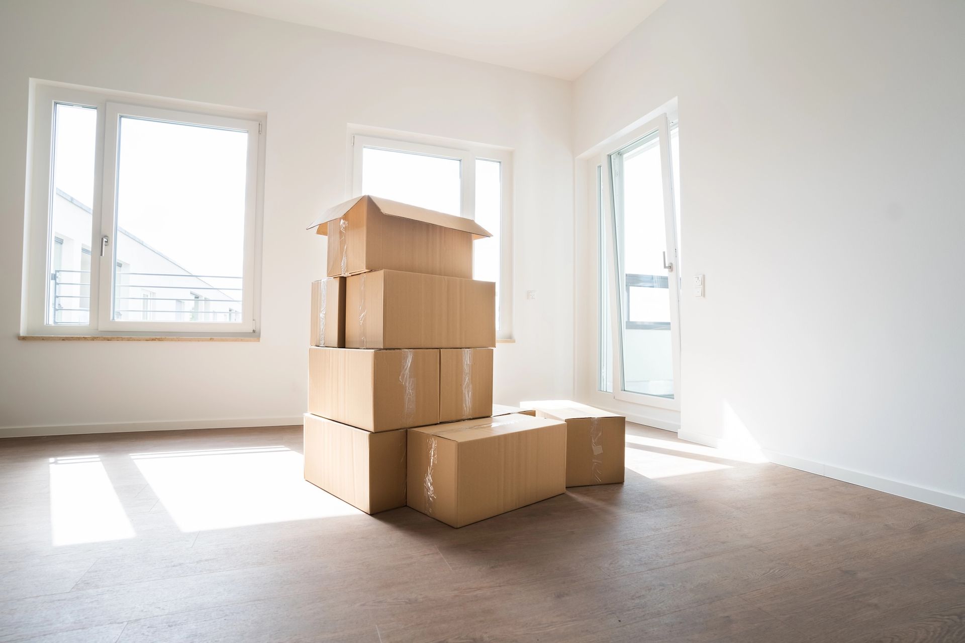 Empty room with wood floors, beige walls, and white trim. Two windows let in light.