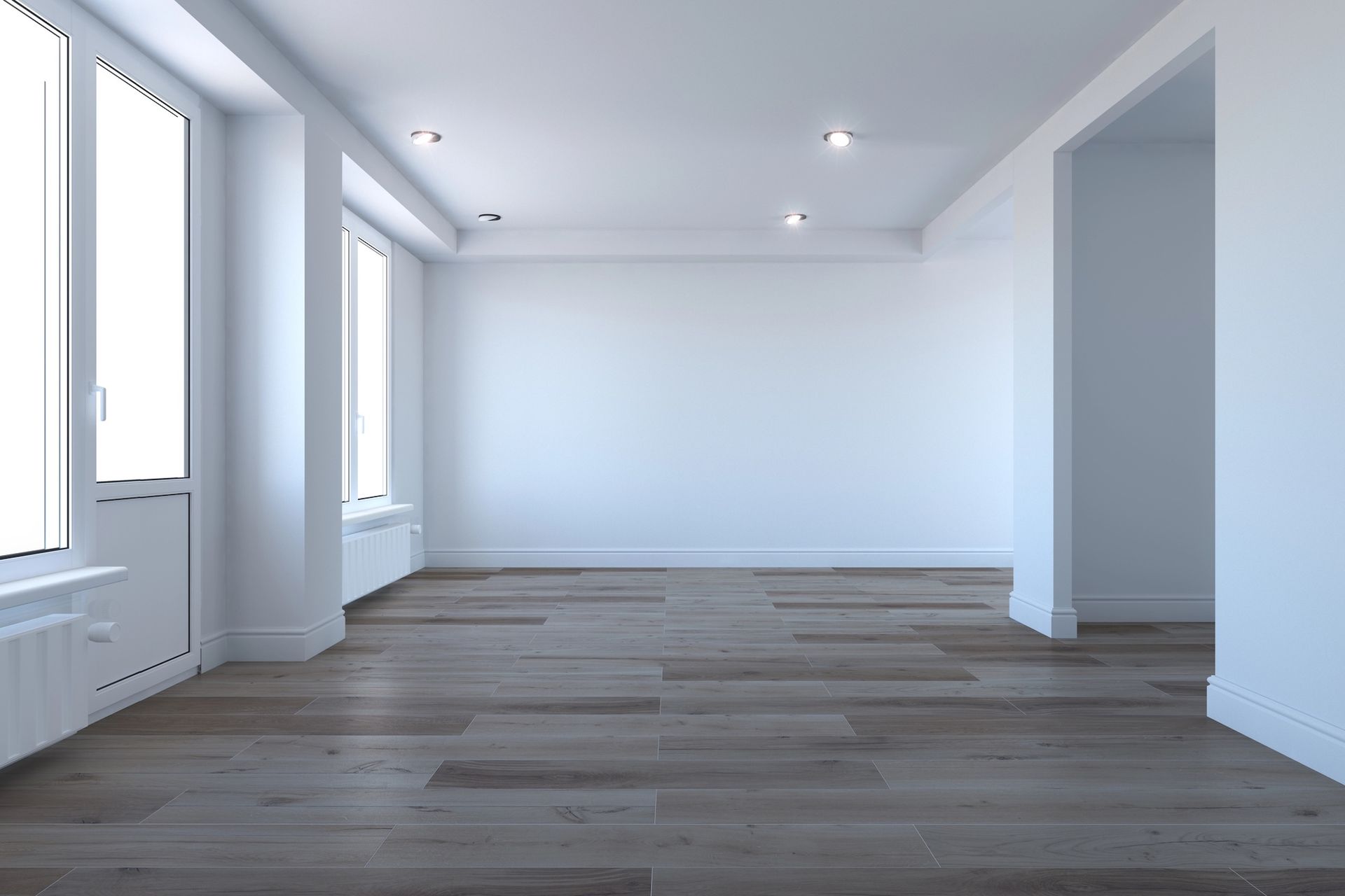 Empty, light-filled room with wood flooring, white walls, and two large windows.