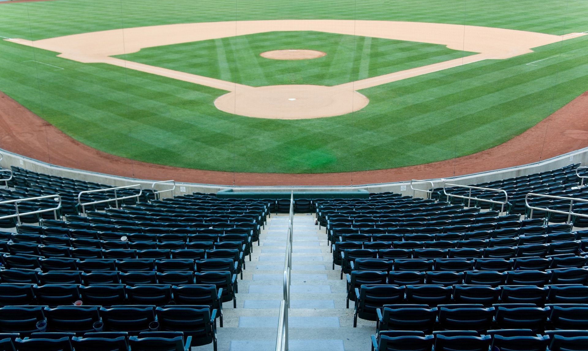 Green stadium seating, metal railings, and concrete supports, with rows of seats under a canopy.