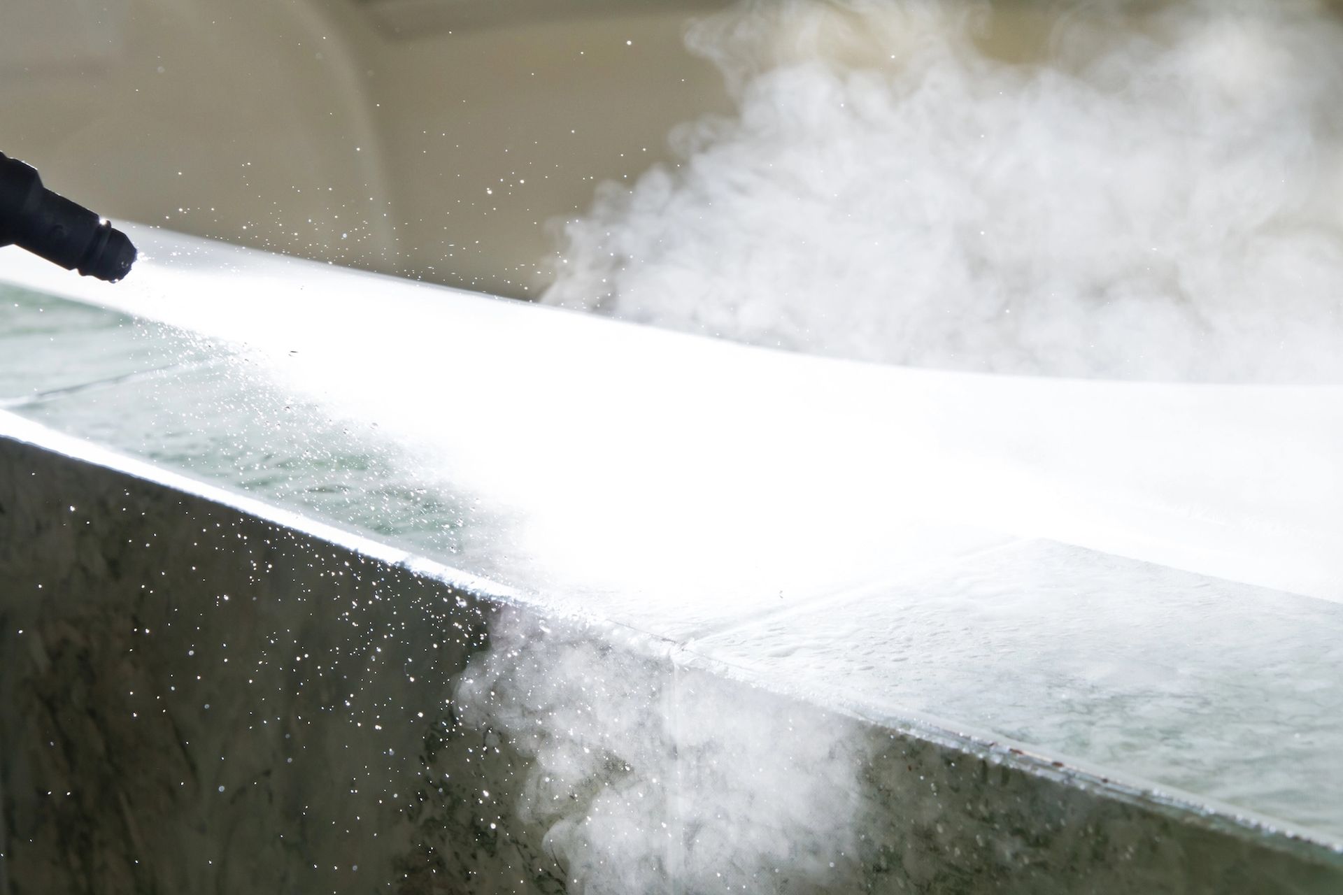 Steam cleaning a gray surface, producing visible vapor.