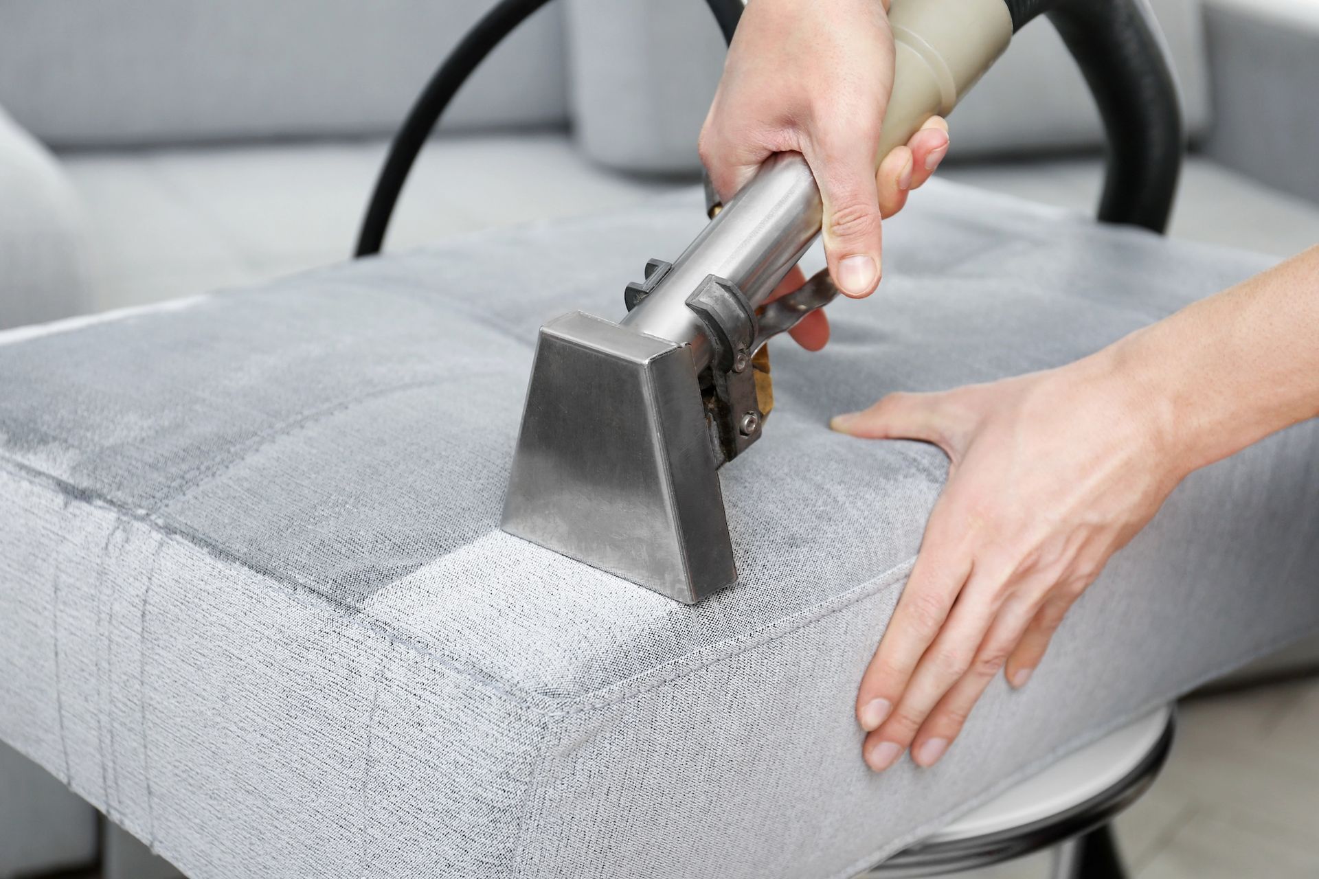 Person using upholstery cleaner on a gray chair cushion.