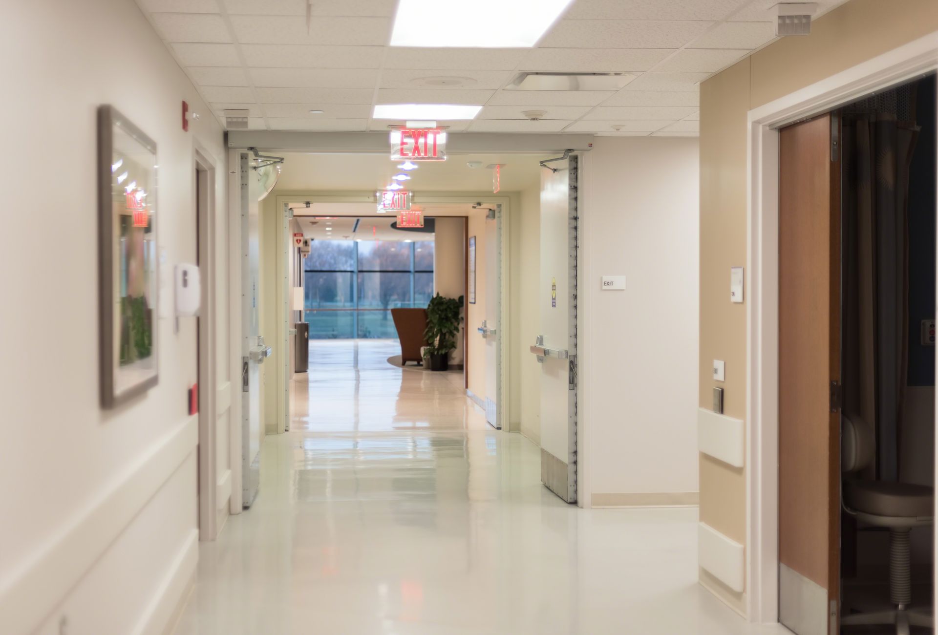 Hospital hallway with open doors, bright lights, and window at the end.