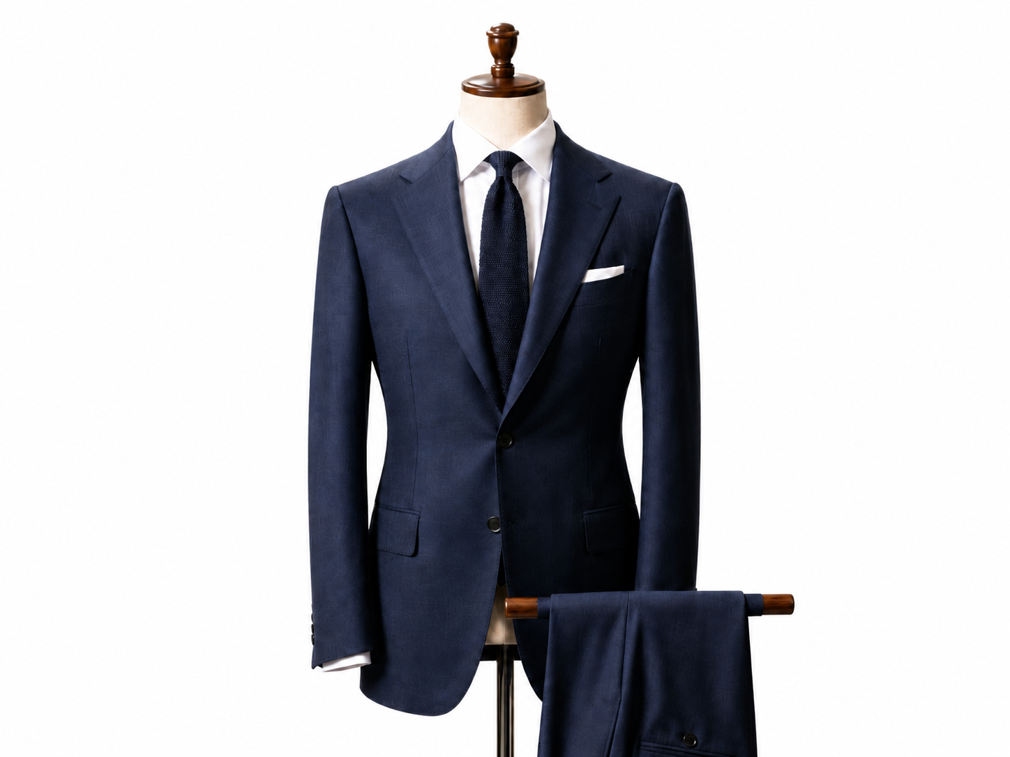 Chaqueta de traje azul marino con corbata y pañuelo de bolsillo a juego en un maniquí, con pantalones drapeados debajo.
