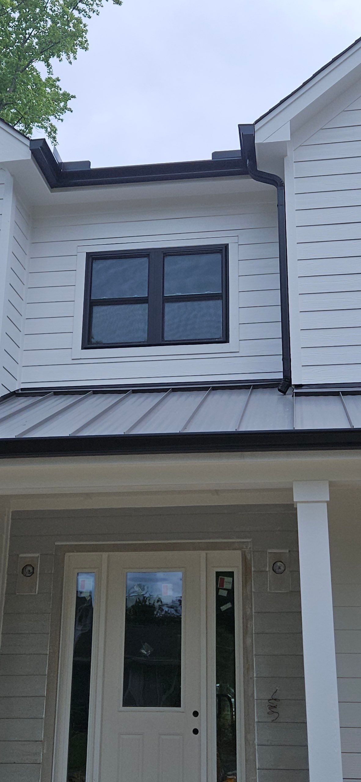 White house exterior with dormer window, front door, and gray metal awning over the entry