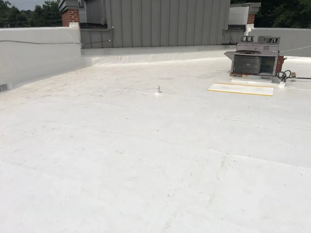 White flat rooftop with a small utility unit and parapet walls under bright sunlight