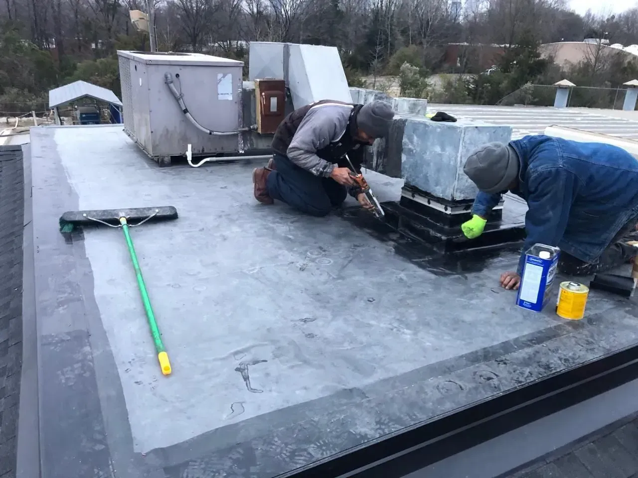Workers repairing a flat rooftop with tools and materials beside HVAC units