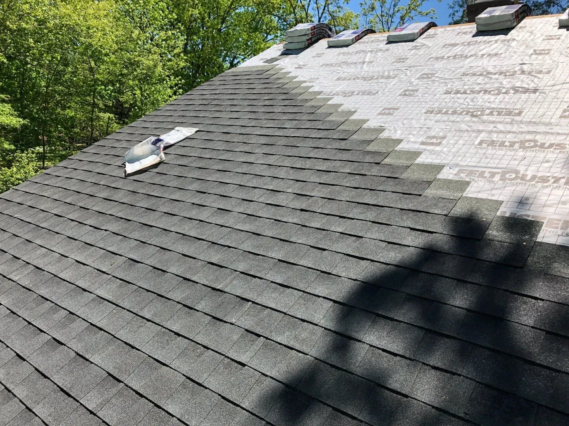 Steep shingled roof with several loose roof vents, trees in the background and shadows across the shingles