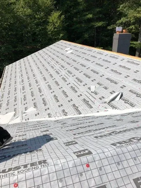 Roof under construction with white underlayment and green trees in the background