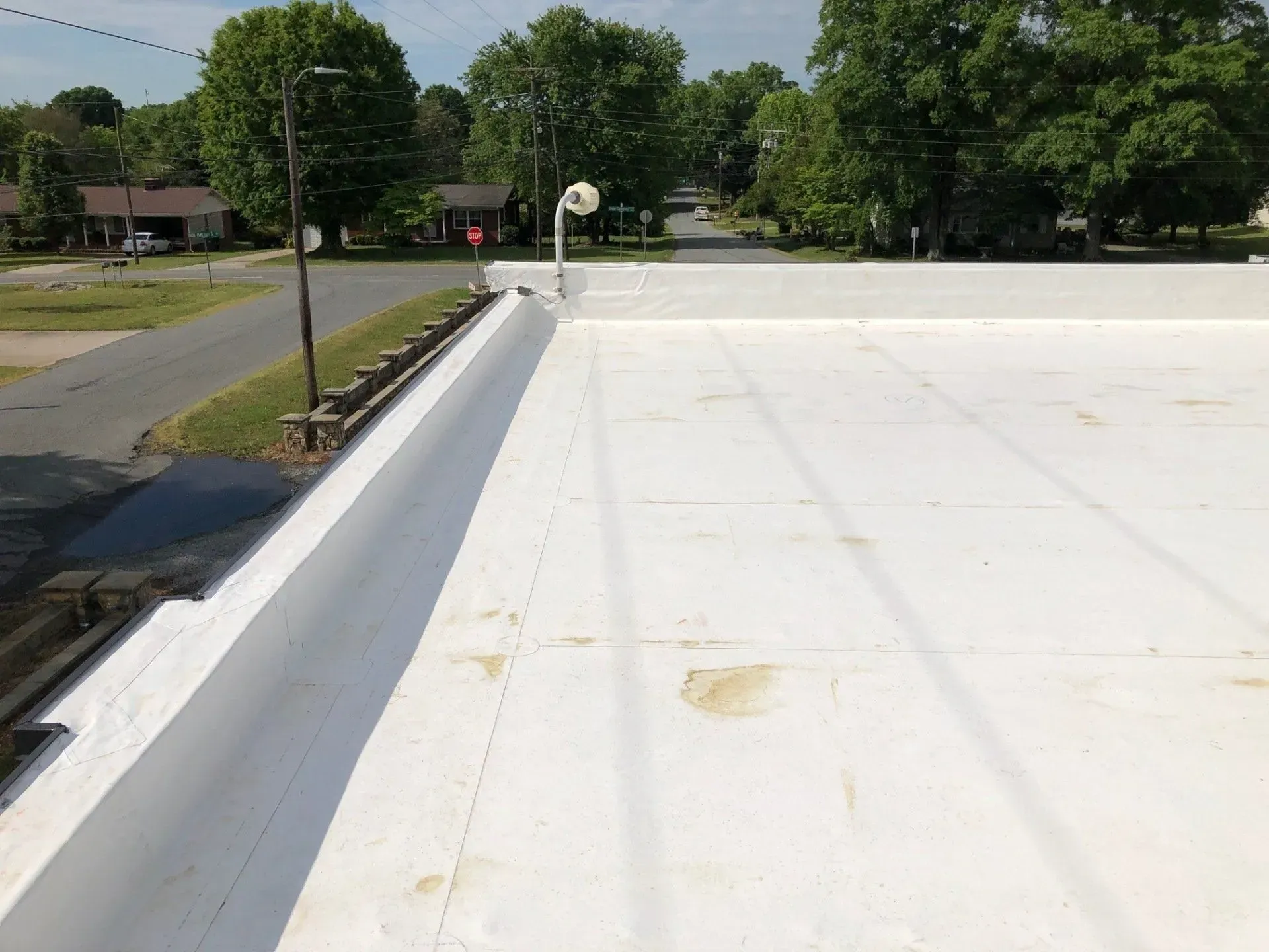 Flat white rooftop with a low parapet beside a road and trees in the distance