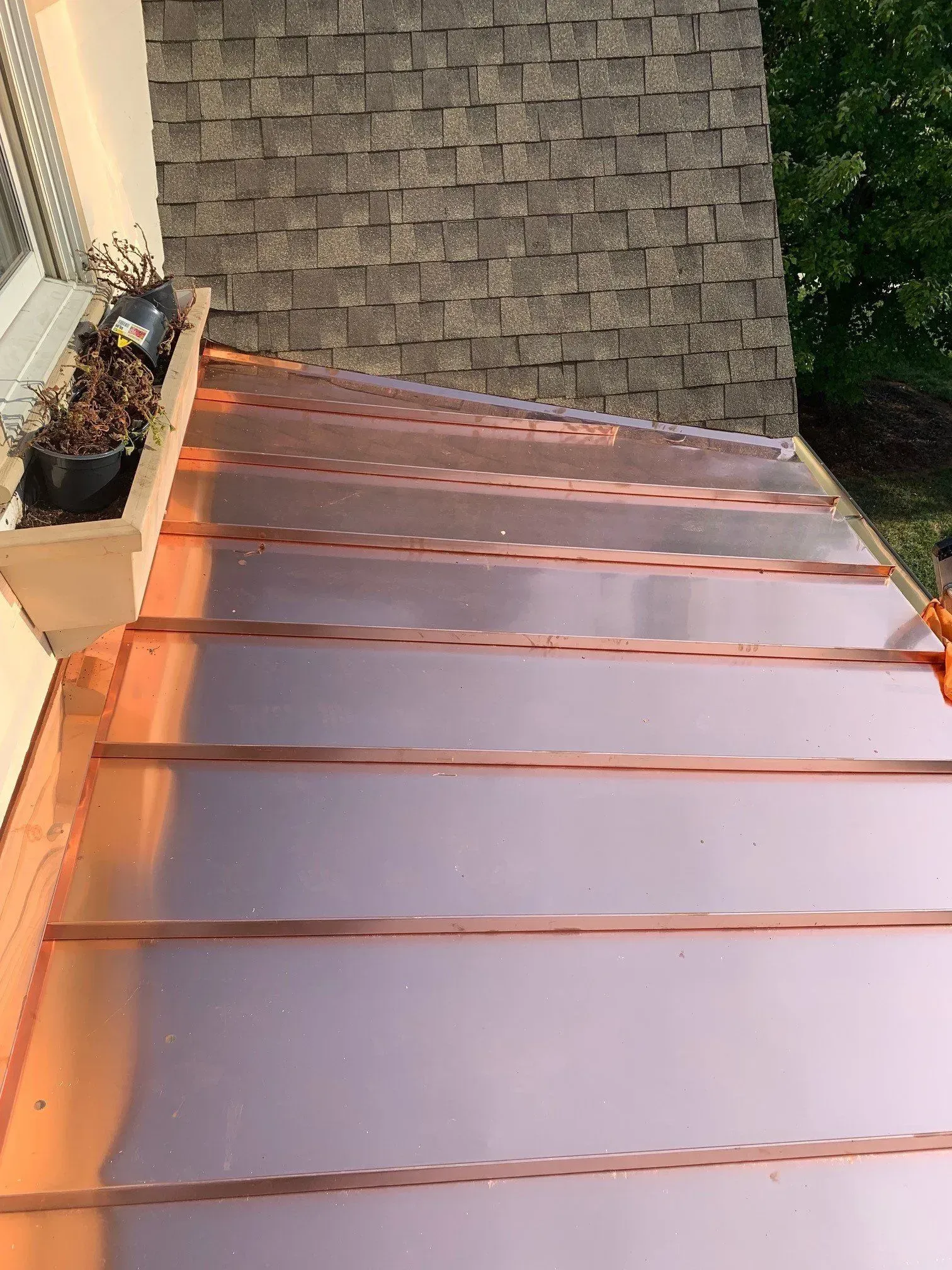 Roof seen from above with reddish panels and shingle sections near a wall and planter