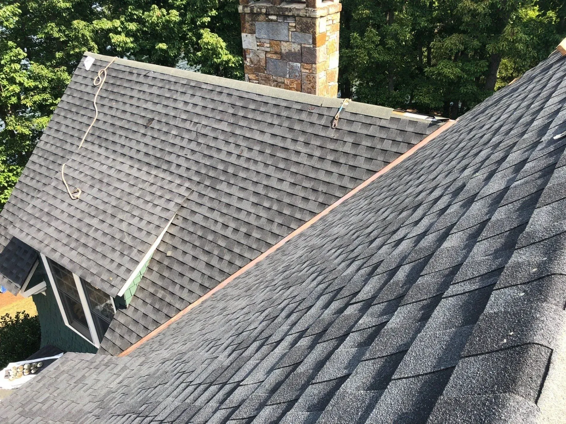 Residential roofs with gray shingles and a brick chimney amid green trees