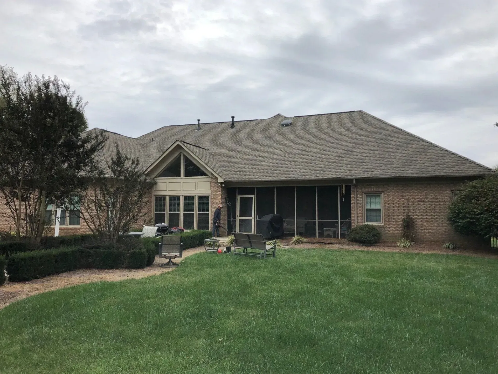 Single-story brick house with a covered front porch and a large green lawn under a cloudy sky