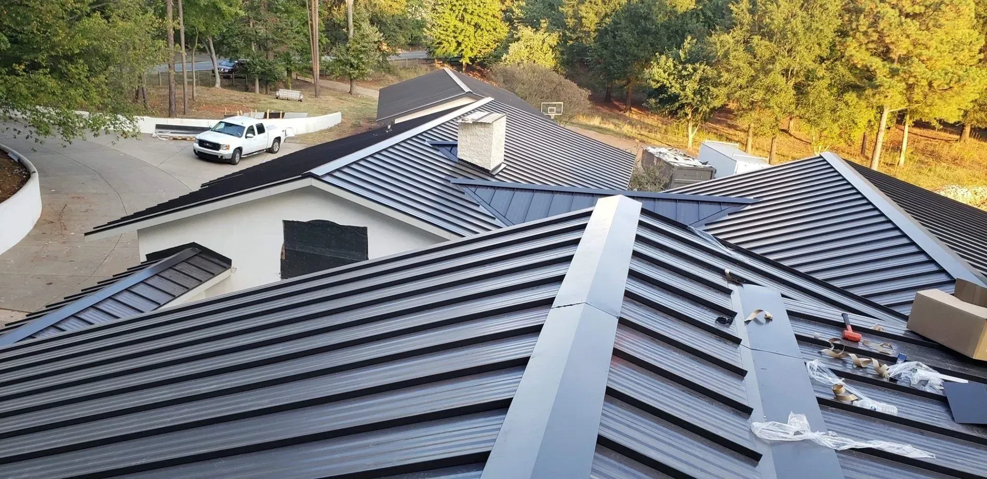 Dark gray metal roof with skylights overlooking trees and parked vehicles near a driveway